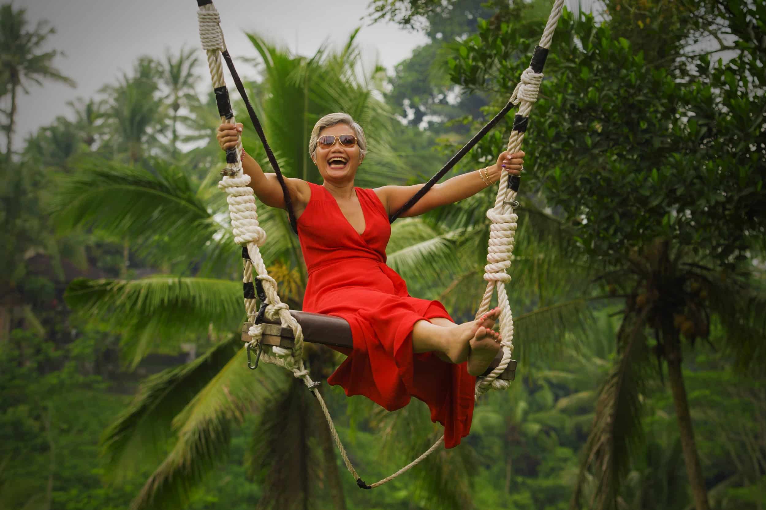 Radiant woman in her 40s joyfully swinging on a rainforest swing