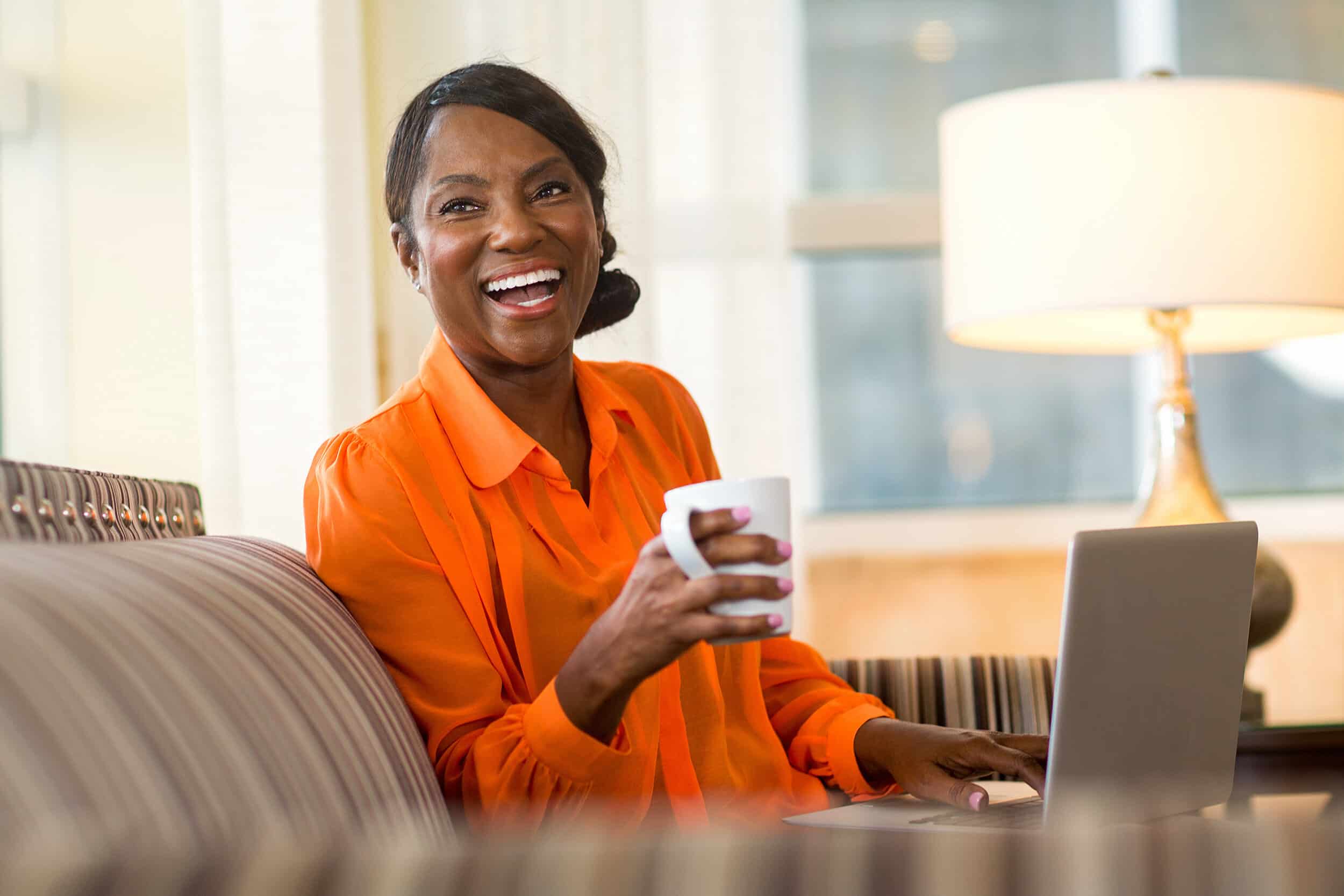 Joyful woman working from home in her computer while enjoying a cup of coffee