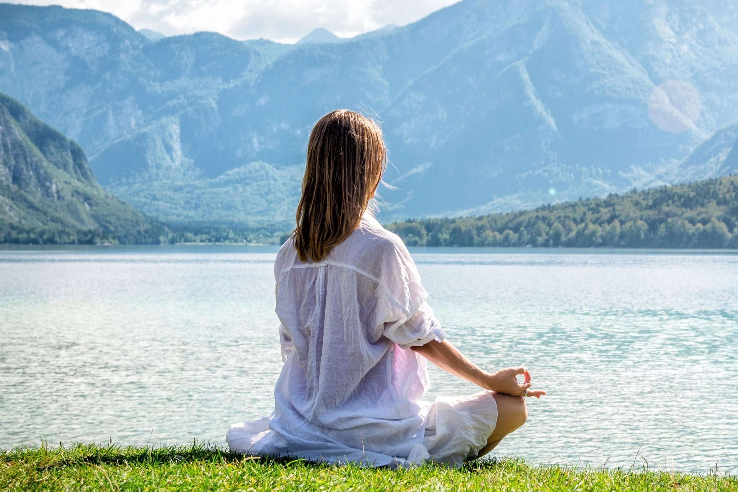 woman in her 40s meditating near the sea and mountains