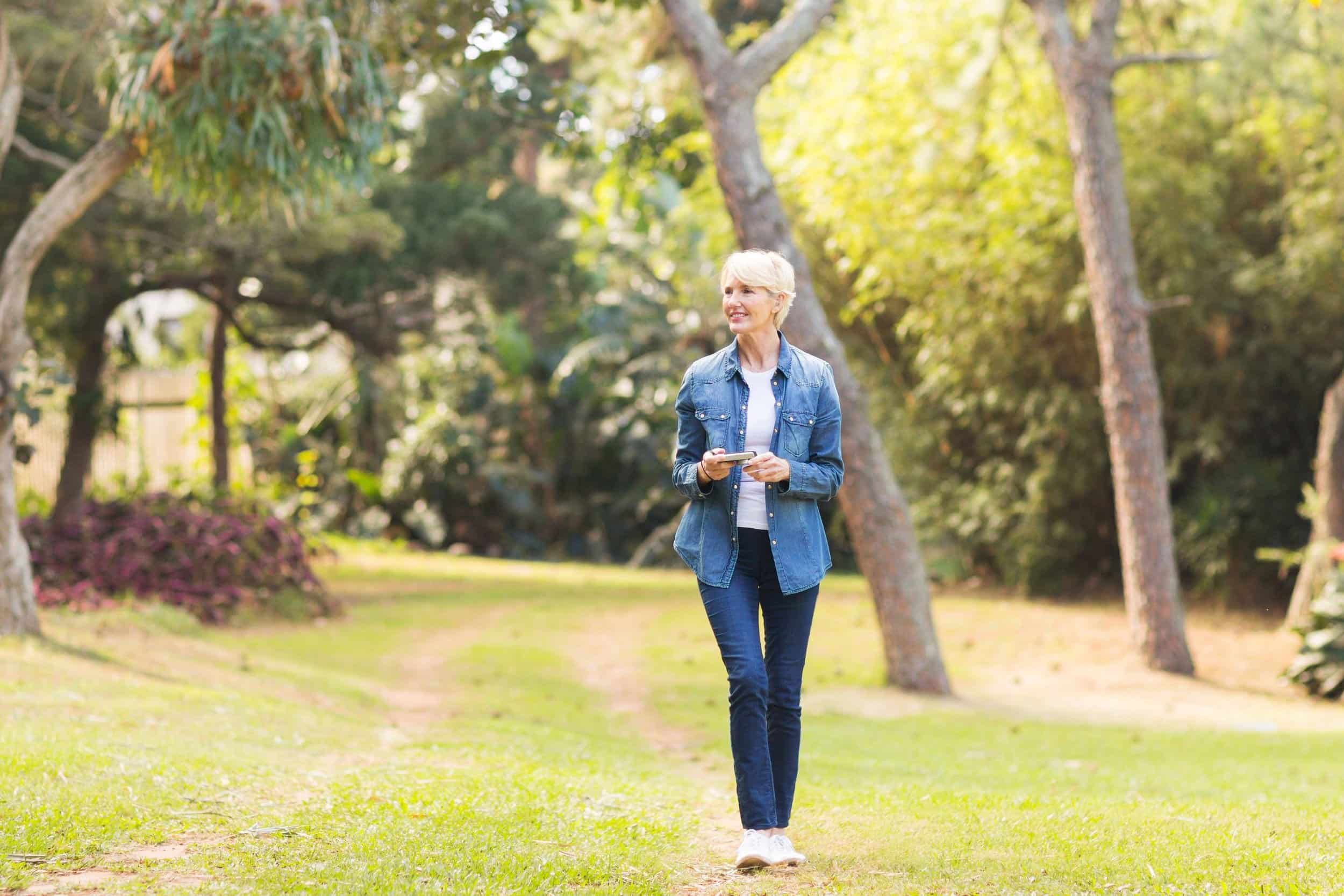 woman in her 50s walking while looking at the plants and trees