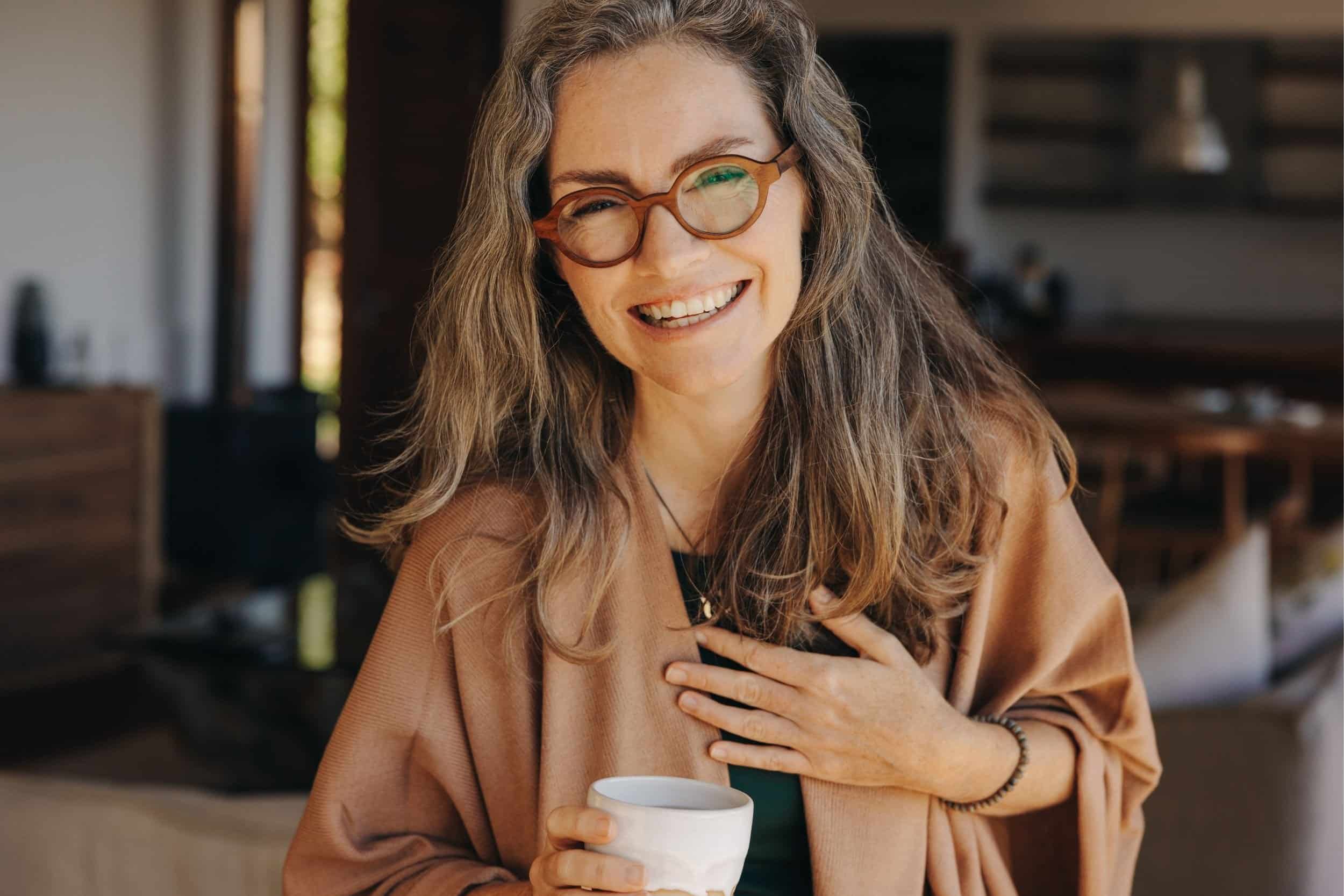 woman in her 40s widely smiling holding a cup of coffee