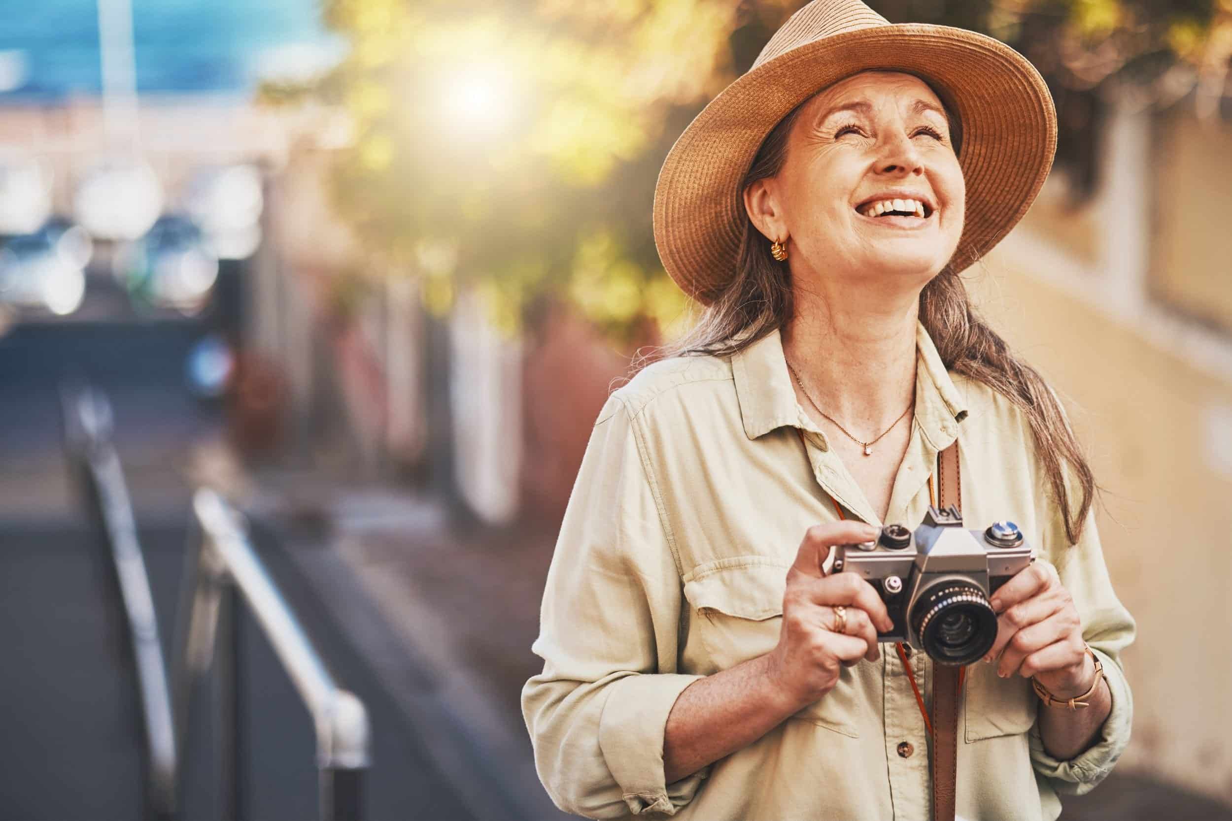 woman in her 40s smiling brightly looking at the sky while holding a vintage camera