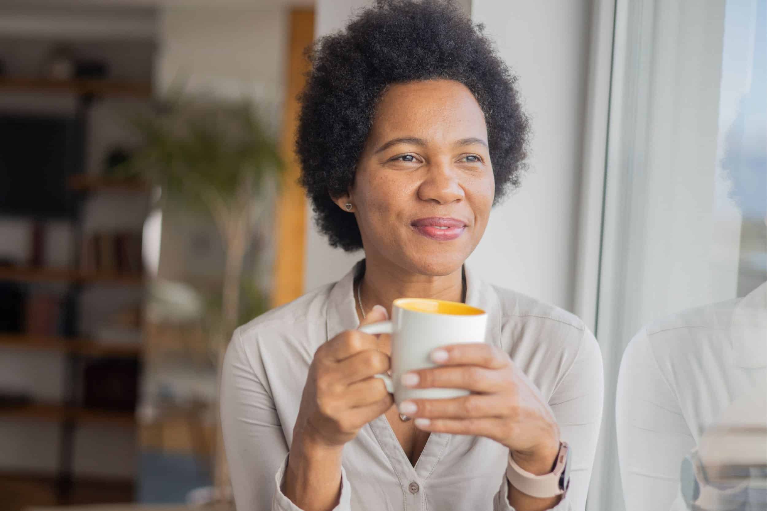 woman wondering while looking in the window holding a cup of coffee